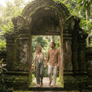 A couple walking hand-in-hand through a beautiful, ancient temple gate in Phuket surrounded by lush greenery, with no other tourists in sight.